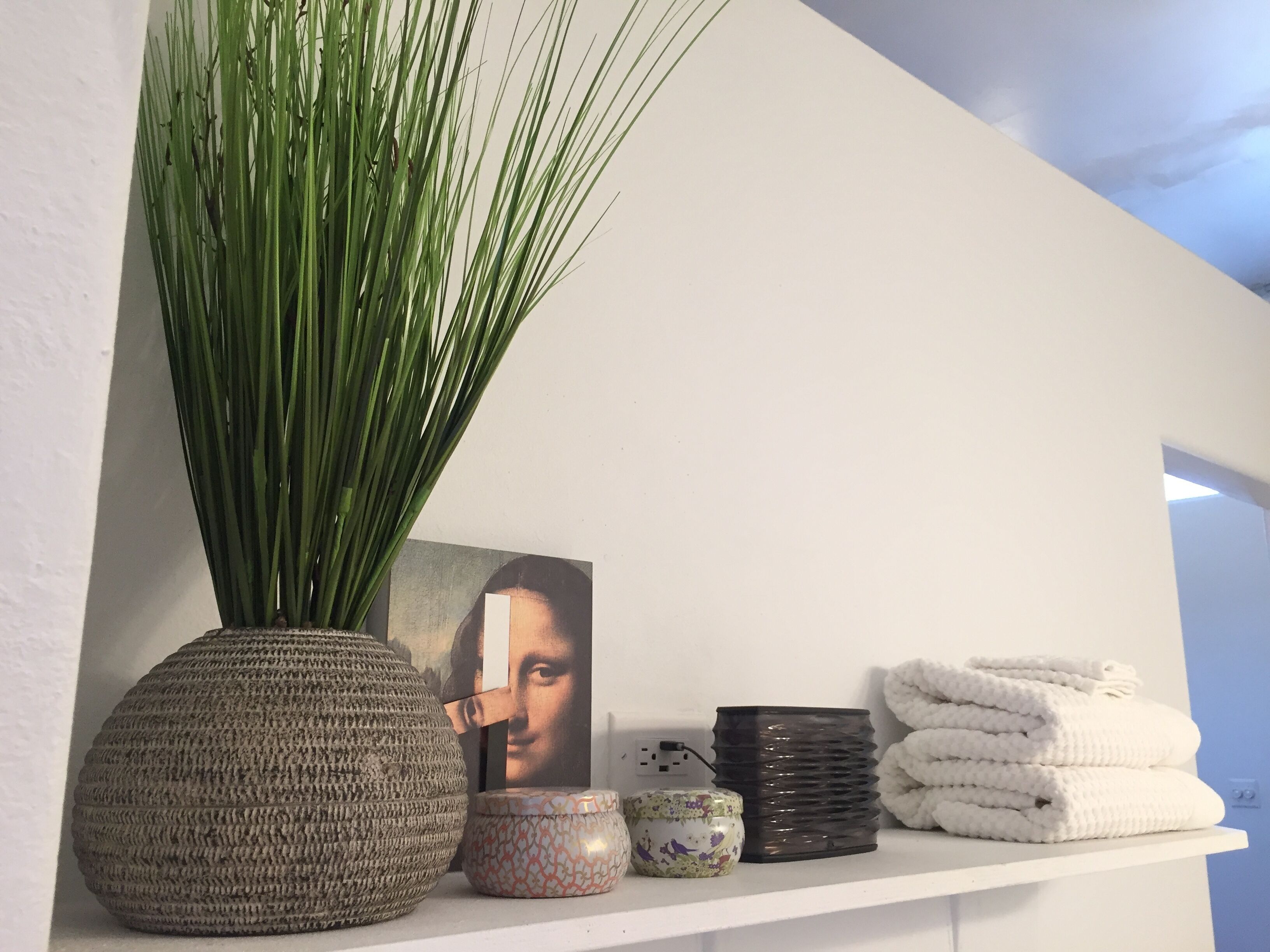A shelf with a woven vase, a patterned container, a black vase, and folded towels.