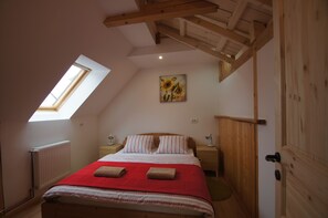 Ein Schlafzimmer mit schrägen Wänden, einem Oberlicht, einem Bett mit roter Bettwäsche, einem Holz-Kopfteil, zwei Nachttischen mit Lampen und einem Gemälde von Sonnenblumen an der Wand.