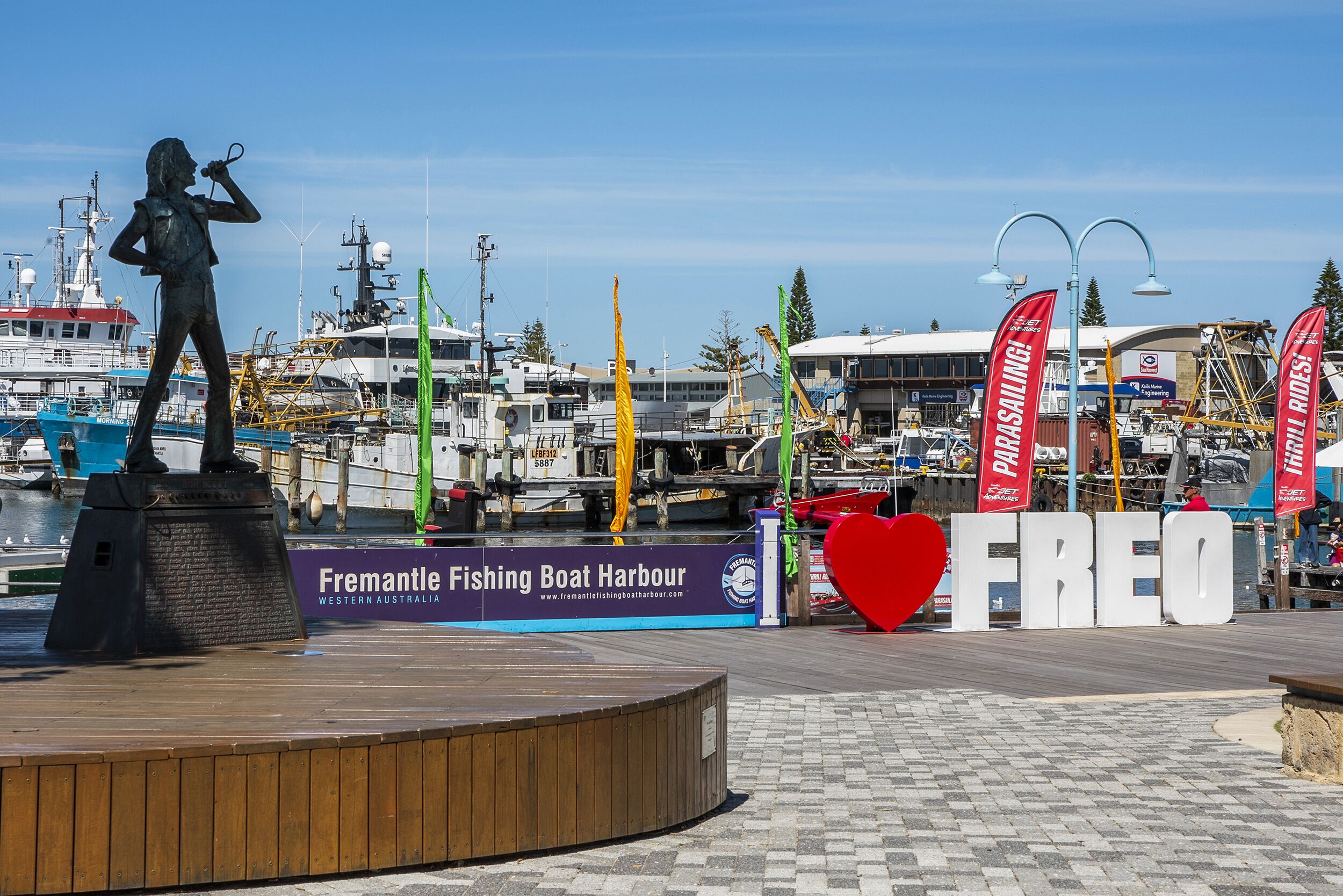 A statue of a woman with a microphone, a sign for Fremantle Fishing Boat Harbour, and a large red heart-shaped sign with the word "FREO".