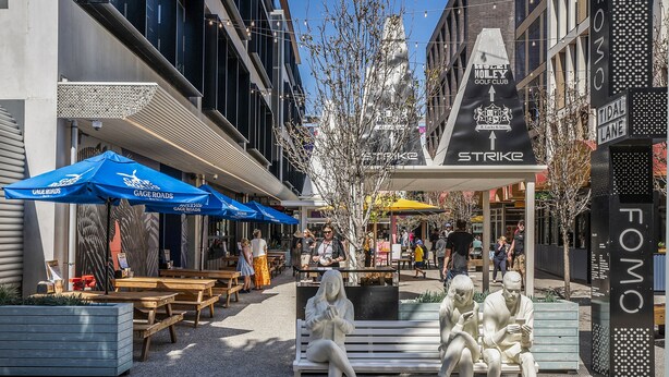 Une rue avec des terrasses, une statue et une enseigne d’hôtel.