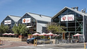 Un bâtiment moderne avec de grandes fenêtres et une enseigne indiquant « The Brew House ». On y voit des parasols à l’extérieur et une voiture garée devant.