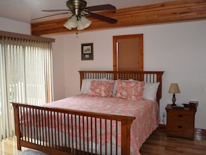 A bedroom with a wooden bed frame, a ceiling fan, a bedside table with a lamp, and a window with blinds.