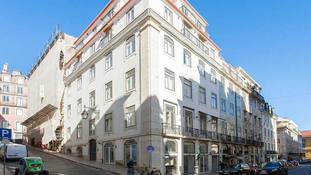 Un immeuble à plusieurs étages, de style architectural classique, qui se distingue par son entrée d’angle imposante et un commerce visible au rez-de-chaussée.