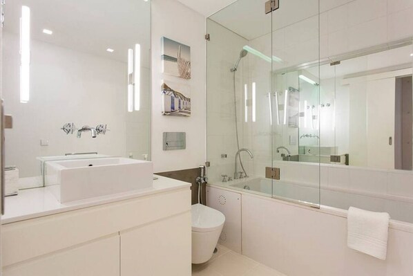 Un baño moderno con un espejo grande, ducha con mampara de vidrio, lavabo blanco y retrete.