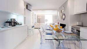 Une cuisine moderne avec une table à manger en verre, des meubles blancs et un coin repas pour le petit-déjeuner.