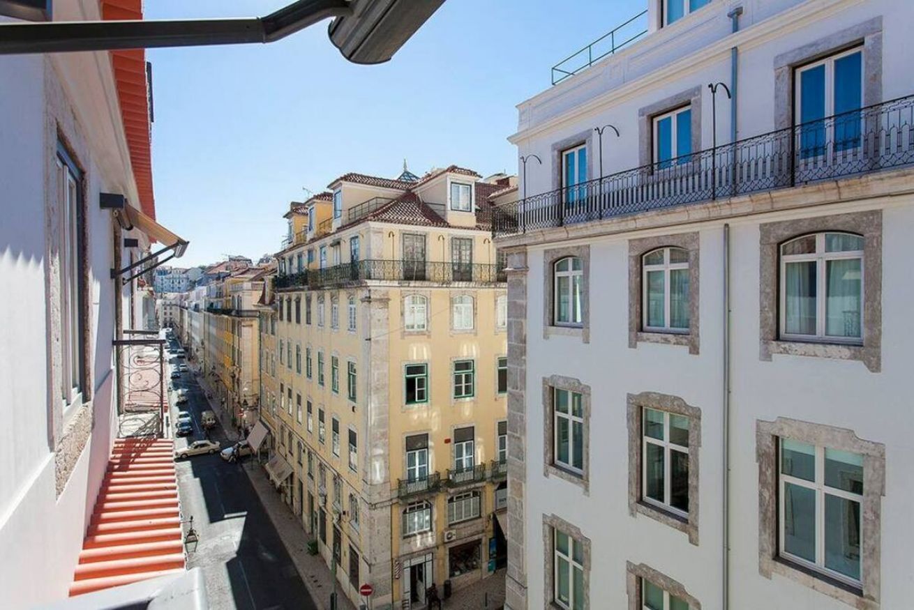 A narrow street with buildings on either side, featuring balconies and multiple stories.