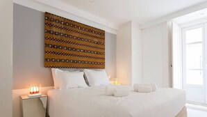 Un lit bien fait, avec du linge de lit blanc, une tête de lit à motifs et des lampes de chevet.