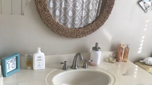 Een badkamer met een wit wastafel, een spiegel met een gevlochten omlijsting, en toiletartikelen op het aanrecht.