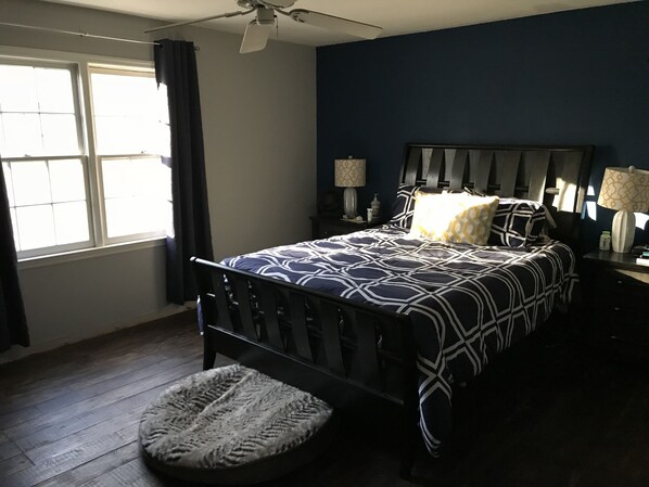 A bedroom with a bed, a nightstand, a lamp, a window with curtains, and a ceiling fan.