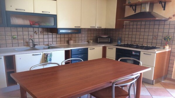 A compact kitchen with a wooden table, two chairs, a sink, a stove, and cabinets.