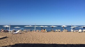 Ein Strand mit Reihen von Liegestühlen und Sonnenschirmen, einem klaren blauen Himmel und dem Ozean im Hintergrund.