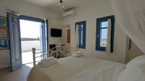 A bedroom with a bed, a TV, a desk, and a chair. There are windows with curtains and a view of the outside. - Villa with private wind-sheltered pool, fab seaviews, walking distance to Beach (Paros)