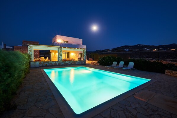 A modern house with a swimming pool, stone patio, and a view of the hills.