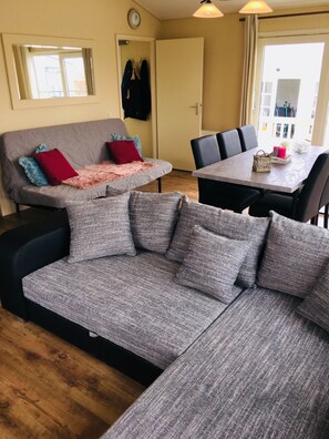 A modern living room with a grey sofa, a dining table, and a large window.