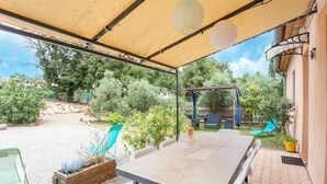 Un patio al aire libre con una mesa y sillas, una pérgola con luces colgantes y vistas al jardín.