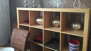 Una estantería de madera con adornos, una silla de mimbre y un cuenco rojo.