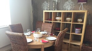 Un comedor con sillas de mimbre, una mesa redonda de madera y un estante con adornos.