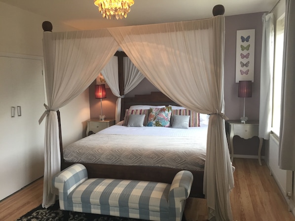 A bedroom with a canopy bed, bedside tables, a bench, and a wall with butterfly decorations.
