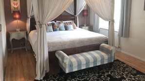 Una cama con dosel y cuatro columnas, con un banco, mesitas de noche y una lámpara fijada a la pared.