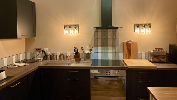 Una cocina moderna con armarios oscuros, horno empotrado, cocina y salpicadero con luces.