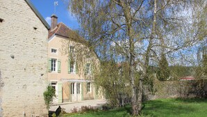 A traditional building with a stone facade, a tiled roof, and a small garden area with a tree and a hedge. - Elegant Family Home in Bouix (Bouix)
