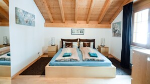 Un dormitorio con techo de madera, una cama grande con ropa de cama a rayas, dos mesitas de noche y obras de arte en las paredes.