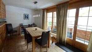 Un comedor con una mesa y sillas de madera, una estantería y un ventanal con cortinas.