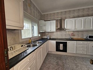 A kitchen with white cabinets, a black countertop, a built-in oven, and a window with blinds.