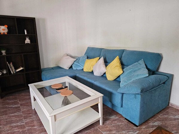 A living room with a blue sofa, a glass coffee table, and a black bookshelf.