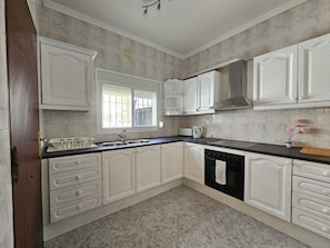 A kitchen with white cabinetry, a black countertop, and a window with blinds.
