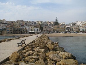 Une promenade en bord de mer, avec une digue rocheuse, des bancs et une rangée de bâtiments en arrière-plan.