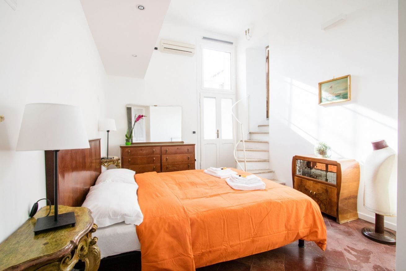 Une chambre à coucher avec un lit, une commode, une chaise, une lampe, un miroir et une fenêtre.