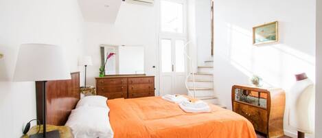 Une chambre à coucher avec un lit, une commode, une chaise, une lampe, un miroir et une fenêtre.