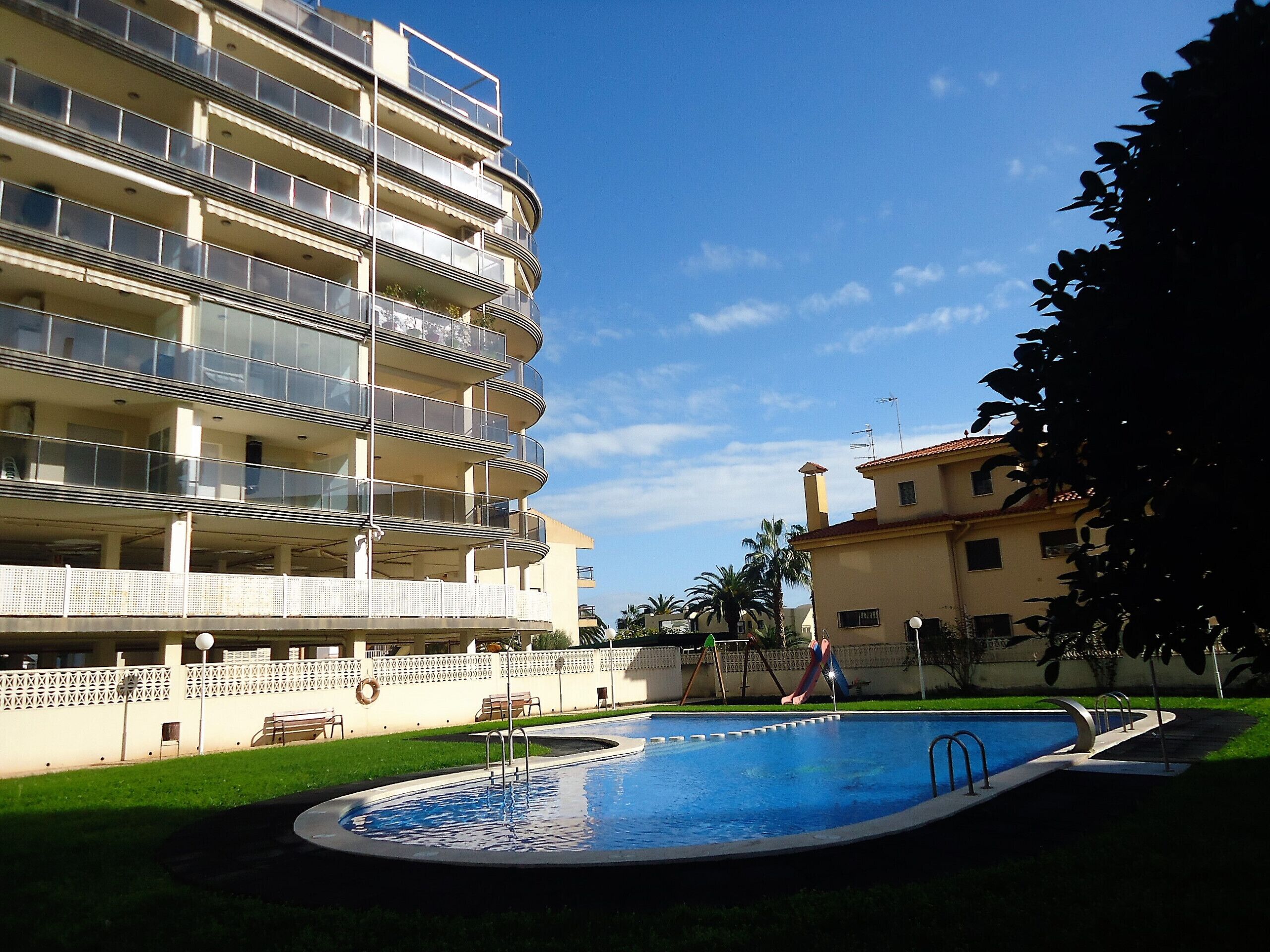 A multi-story building with balconies, a swimming pool, and a playground.