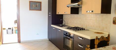 A kitchen with a gas stove, oven, and dark cabinets. There is a window with a view of the outside.