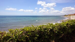 Une vue sur la côte, avec un ciel dégagé, une mer calme et, au loin, un bâtiment à la façade blanche.