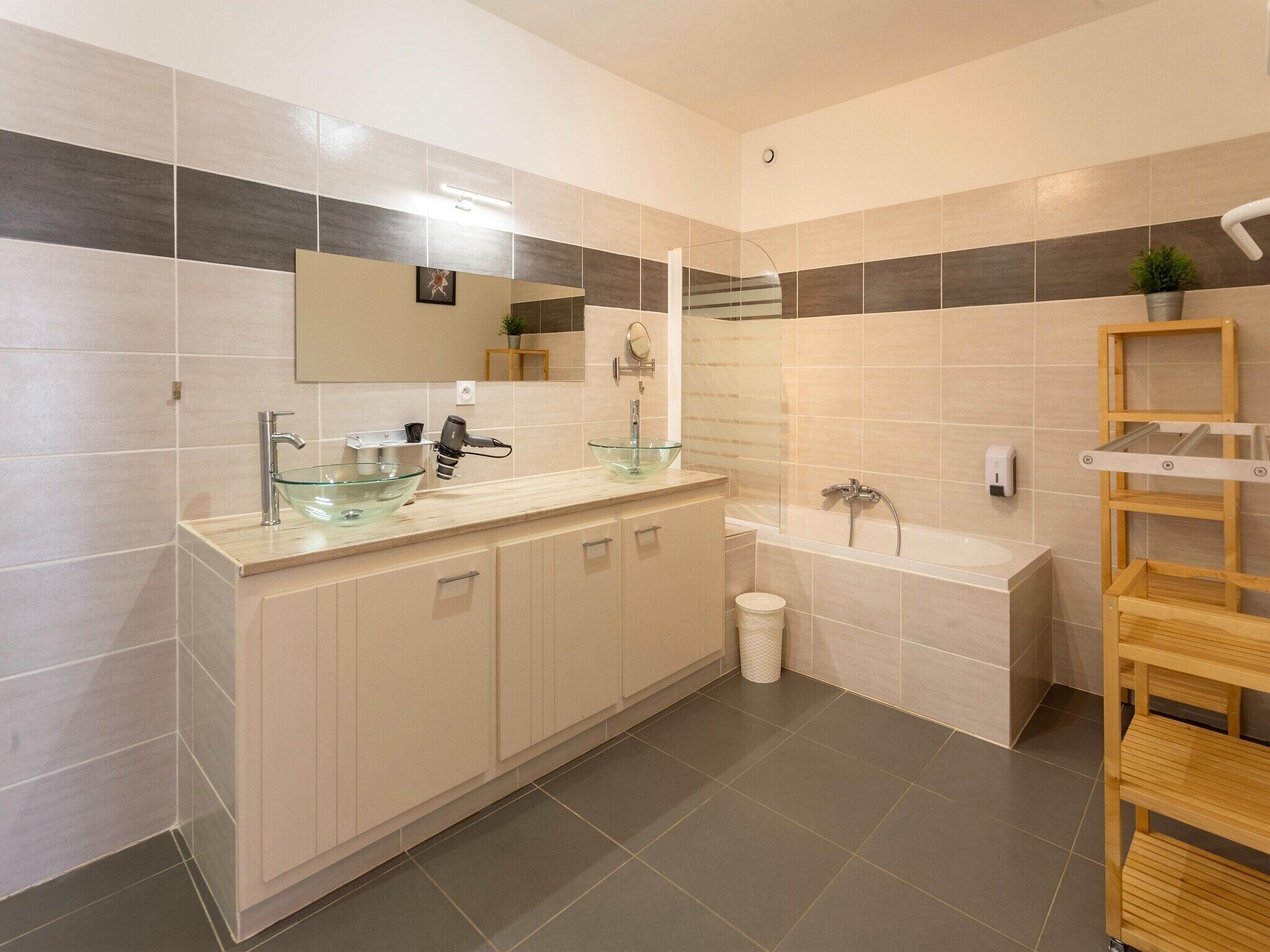 A modern bathroom with a glass basin sink, a shower, and a wooden shelf.