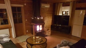 A cozy living room with a wooden interior, a round table with a bottle and glasses, and a dog lying on a couch. - Näset 4 Green Cabin in Småland with boat (Vena)