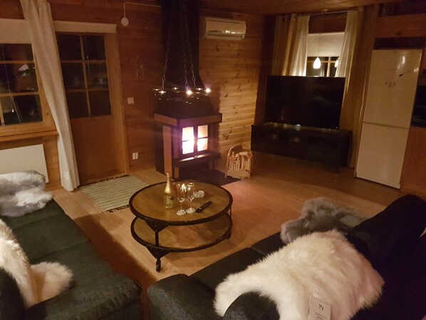 Ett mysigt vardagsrum med träinredning, ett runt bord med en flaska och glas, och en hund som ligger på en soffa.
