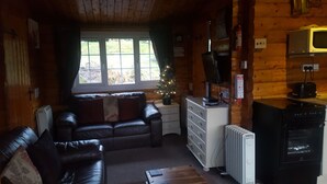 A cozy cabin interior with a leather sofa, a small wooden table, a radiator, and a Christmas tree.