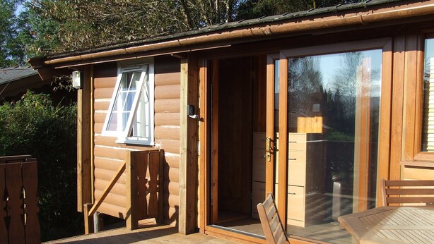 A wooden cabin with a sliding glass door, a small deck, and a table and chair set. - SNOWDONIA LOG CABIN RETREAT 4 BERTH FAMILY/PET FRIENDLY. STUNNING MOUNTAIN VIEWS (Trawsfynydd)