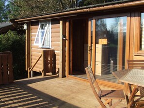 Eine Holzhütte mit Schiebetür, einer kleinen Terrasse und einem Tisch mit Stühlen.