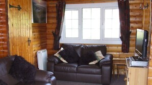 A cozy log cabin interior with a leather sofa, a television, and a small wooden table. - SNOWDONIA LOG CABIN RETREAT 4 BERTH FAMILY/PET FRIENDLY. STUNNING MOUNTAIN VIEWS (Trawsfynydd)