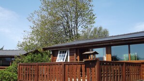 A wooden cabin with a balcony, large windows, and a view of trees. - SNOWDONIA LOG CABIN RETREAT 4 BERTH FAMILY/PET FRIENDLY. STUNNING MOUNTAIN VIEWS (Trawsfynydd)