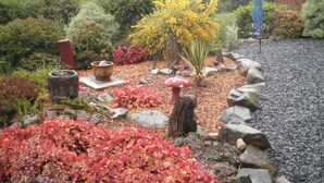 A garden with various plants, a decorative mushroom, and a wooden structure in the background. - SNOWDONIA LOG CABIN RETREAT 4 BERTH FAMILY/PET FRIENDLY. STUNNING MOUNTAIN VIEWS (Trawsfynydd)