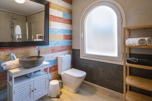 Ein Badezimmer mit einem großen Spiegel, einem Aufsatzwaschbecken, einer Toilette und einem Holzregal mit Handtüchern.