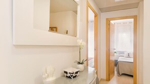 Un couloir d’hôtel avec un miroir, une petite plante et un cactus posés sur une console grise.