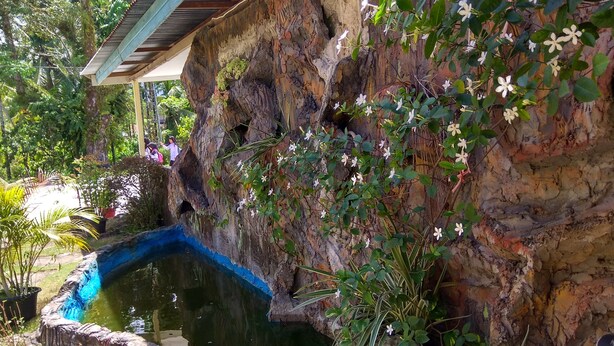 A rock garden with a small pond, lush greenery, and a wooden structure. - Malompek (Padang)