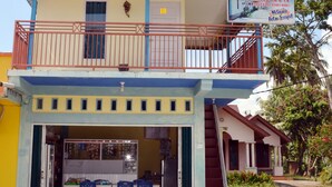 A two-story building with a balcony, a sign advertising AC and TV facilities, and a small outdoor seating area with blue chairs. - Malompek (Padang)