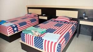 A hotel room with two beds, each adorned with American flag bedding. There are bedside tables with lamps and a small drawer. - Malompek (Padang)